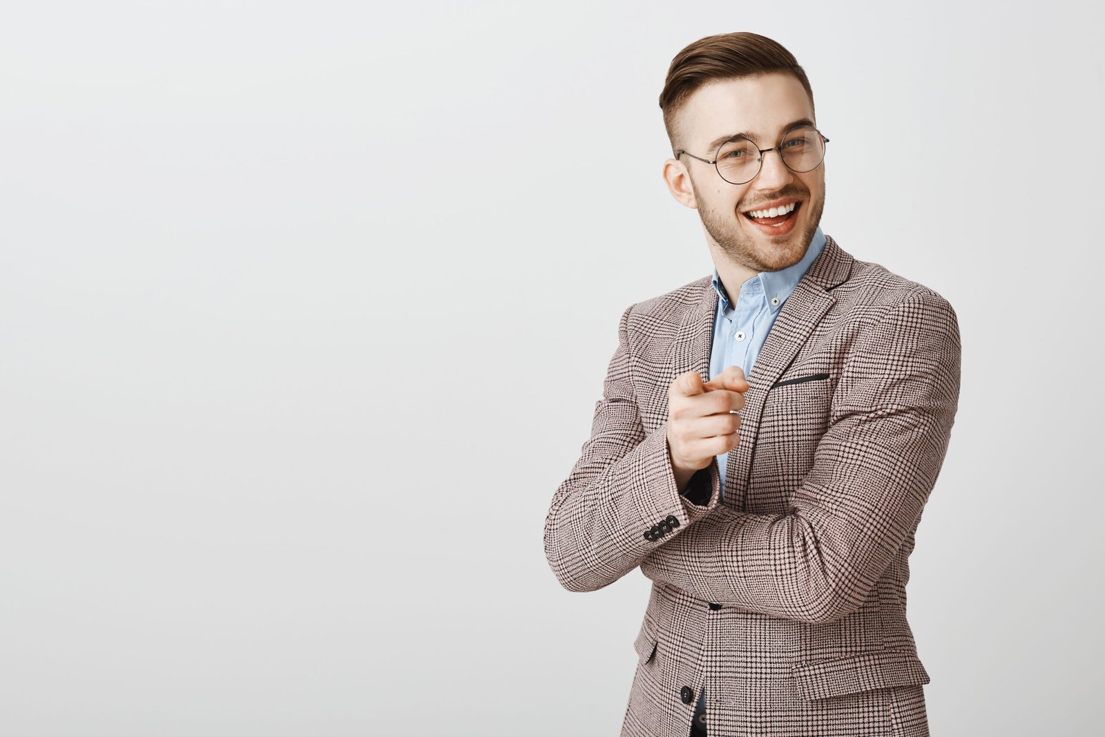 Your ideas promising Pleased and delighted smart businessman in trendy formal jacket and glasses smiling and pointing at camera as if agreeing and liking interesting plan over gray background